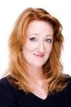 Amanda Alexander headshot photo, smiling woman with red hair wearing black top in front of white background