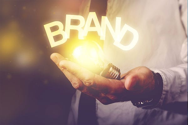 person holding a lit lightbulb in their hand with the word BRAND over it