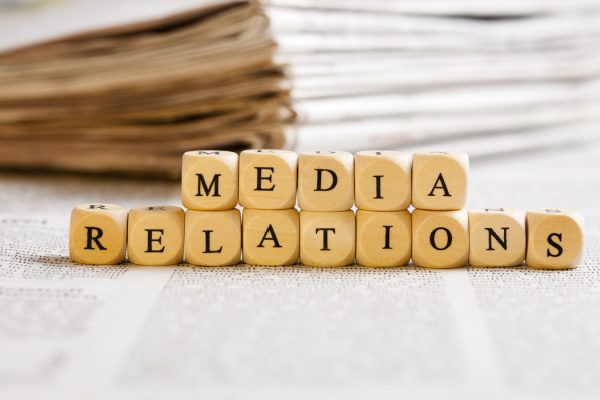 small blocks in front of a stack of news paper spelling Media Relations