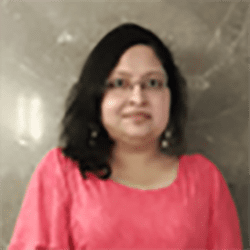 Saimantee Bhattacharya ACC headshot photo, dark haired woman smiling in a pink top standing in front of a marble wall